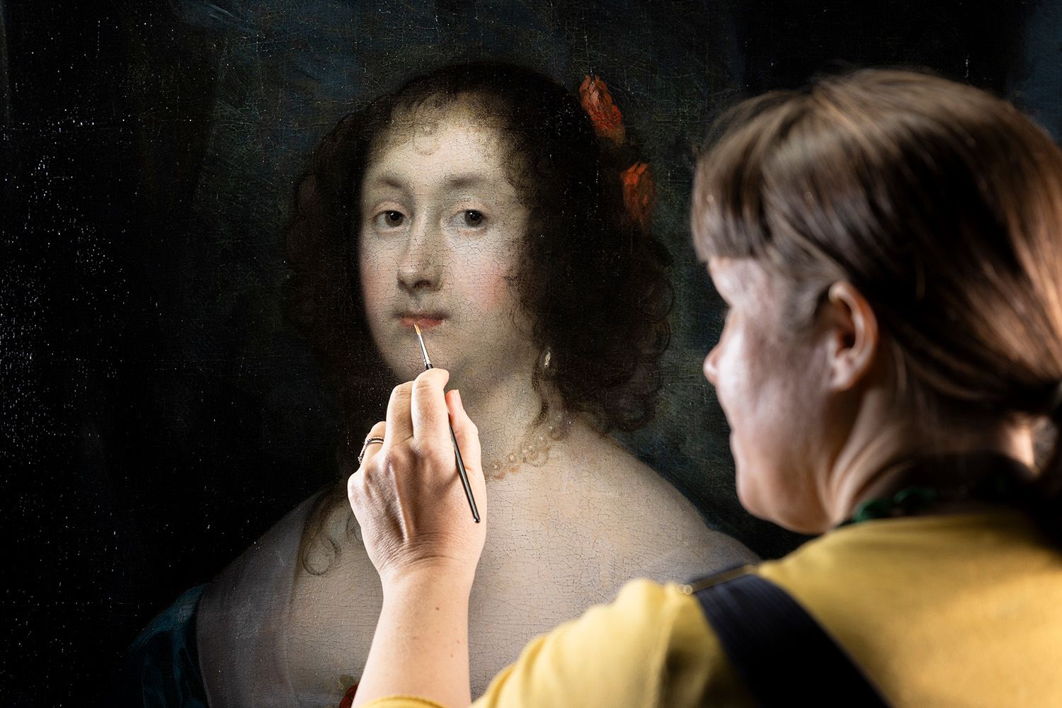 A restorer works on the lips of the Diana Cecil portrait with a tiny brush.
