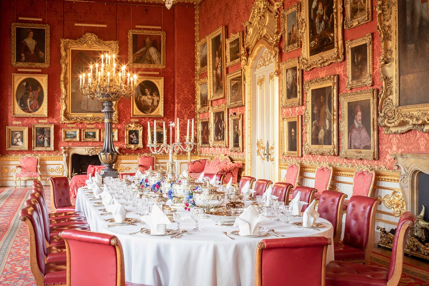 A photo of a large room at Apsley House showing a table set for a stately dinner, and many paintings on the deep red walls with gold frames.
