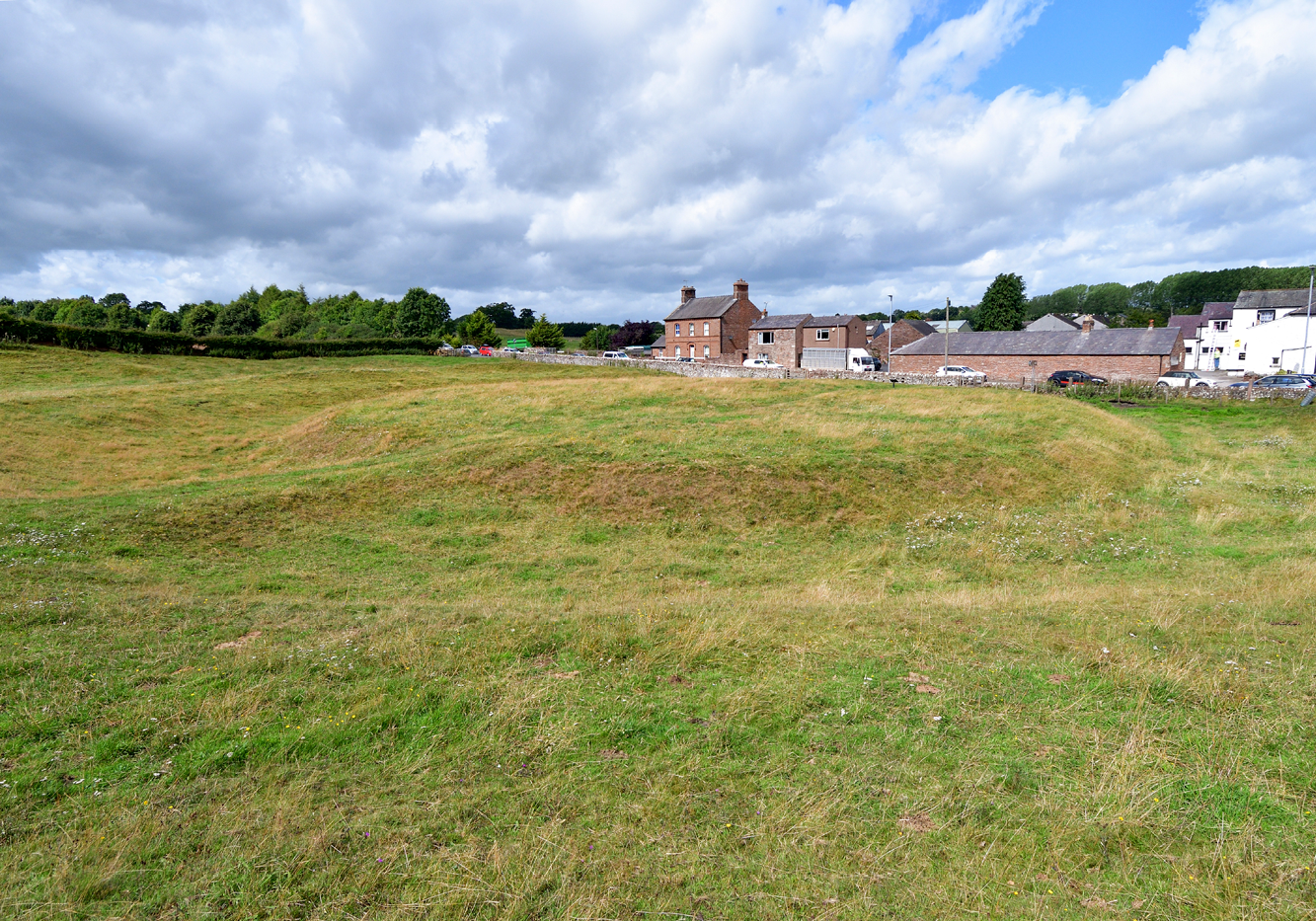 An aerial view of a round earthwork in the field next to a village 